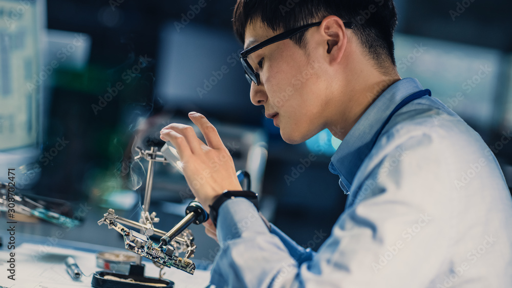 身穿蓝色衬衫的日本专业电子开发工程师正在焊接电路板