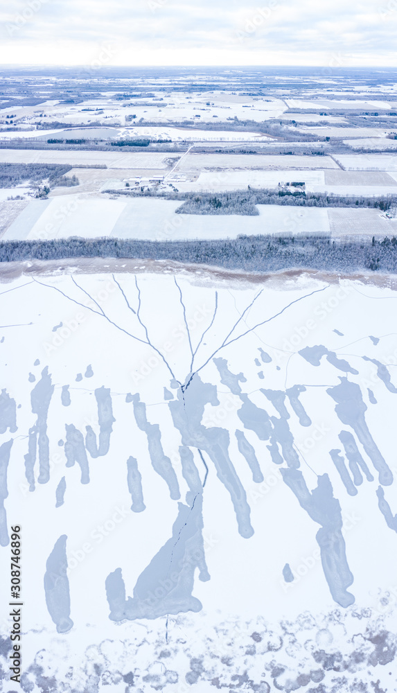 Aerial drone view of a partially frozen lake with unfrozen patches and ice cracks on a winter mornin