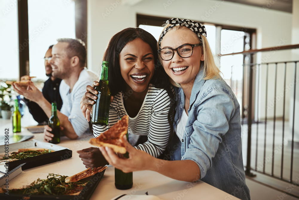 Laughing businesswomen having beers and pizza with colleagues af
