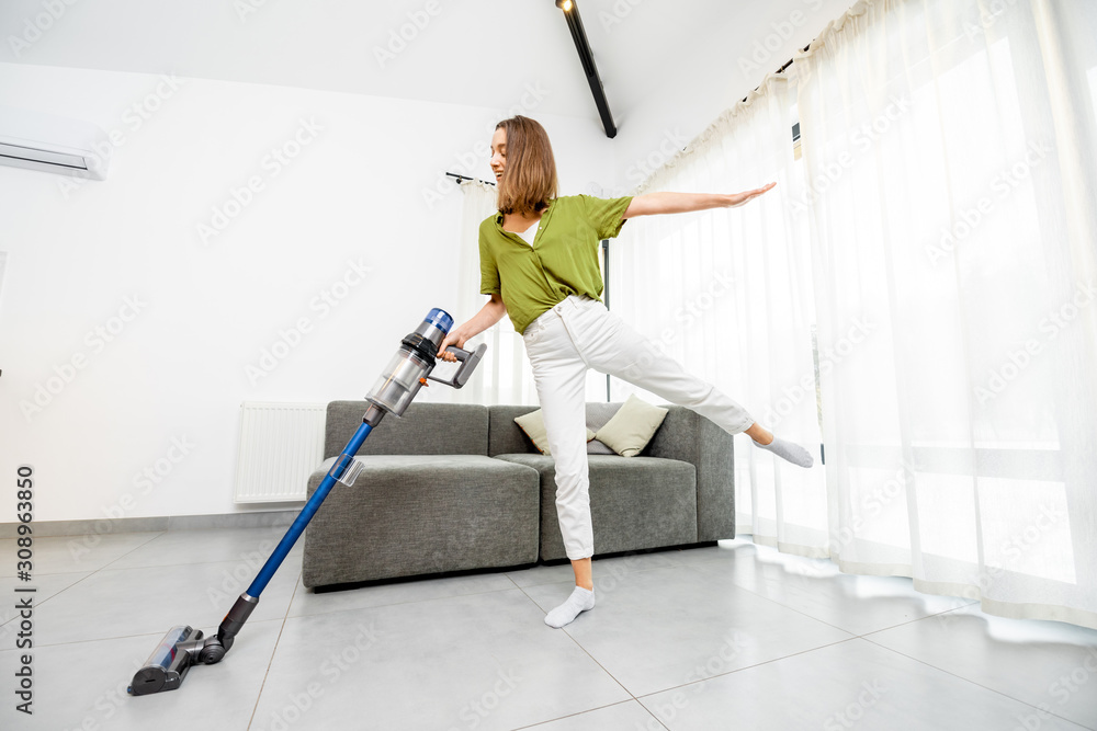 年轻女性享受家务，穿着现代白色livi用无绳吸尘器清洁地板