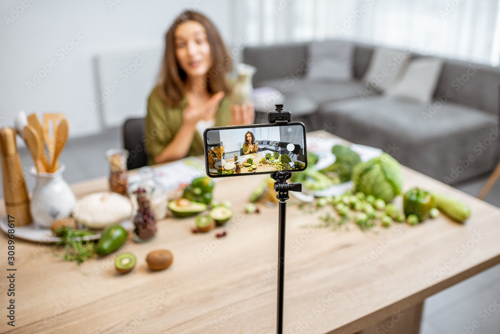 一位年轻女士在智能手机上录制了她关于健康饮食的视频日志。坐在桌子旁。