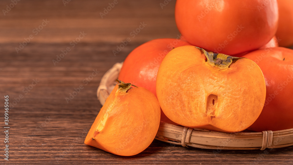 Sliced sweet persimmon kaki in a bamboo sieve basket on dark wooden table with red brick wall backgr