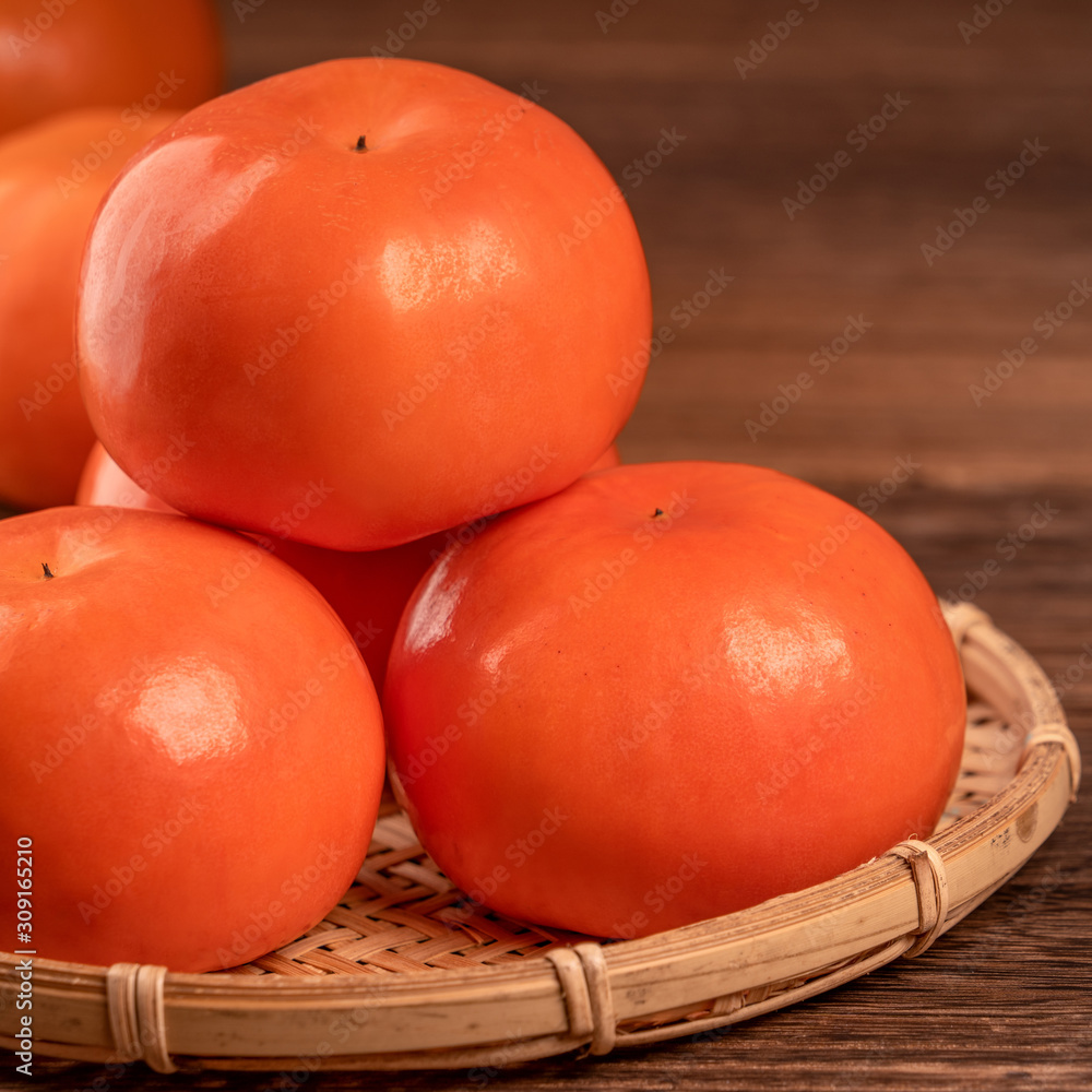 Sliced sweet persimmon kaki in a bamboo sieve basket on dark wooden table with red brick wall backgr