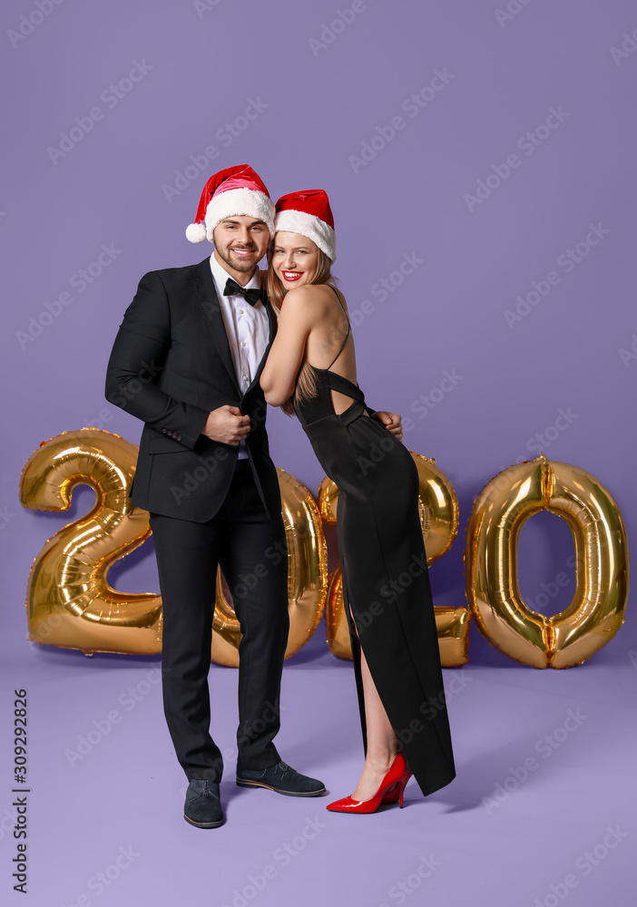 Happy couple in Santa Claus hats on color background