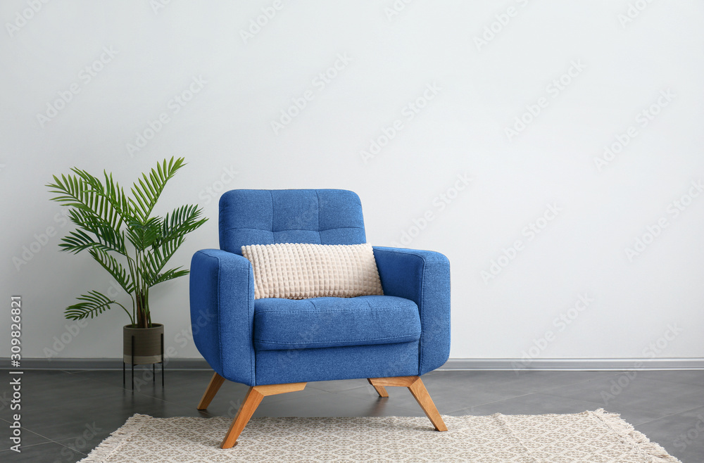 Comfortable blue armchair and houseplant near light wall