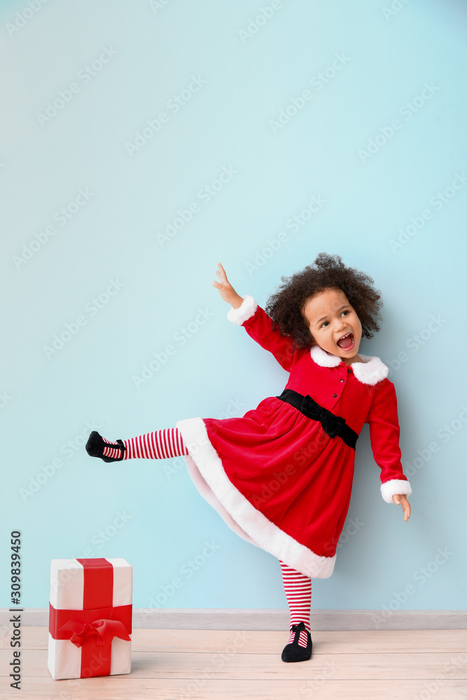 彩色墙附近穿着圣诞老人服装的非洲裔小女孩