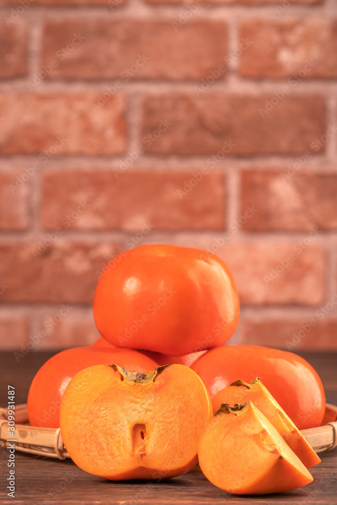 红色砖墙背景深色木桌上新鲜漂亮的甜柿子片，Chi
