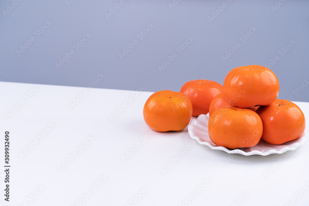新鲜漂亮的甜柿子片隔离在白色厨房桌子上，背景是灰蓝色