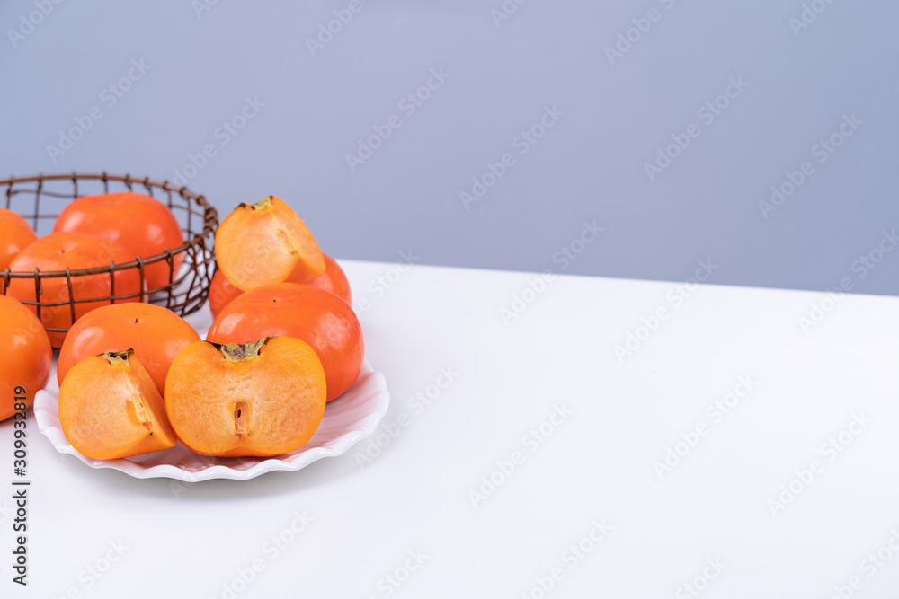 新鲜漂亮的甜柿子切片，隔离在白色厨房桌子上，背景为灰蓝色