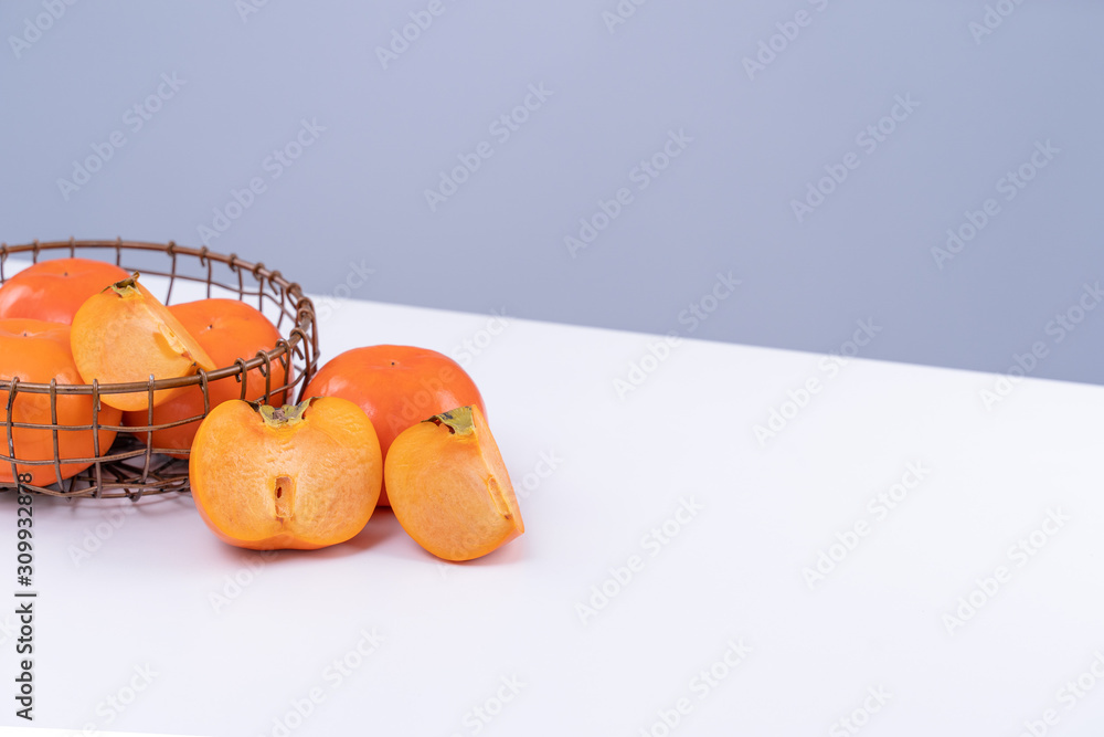 新鲜漂亮的甜柿子切片，隔离在灰蓝色背景的白色餐桌上