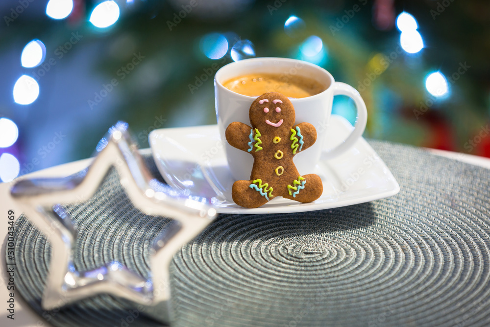姜饼饼干人在一杯热咖啡旁，背景是圣诞树的灯光