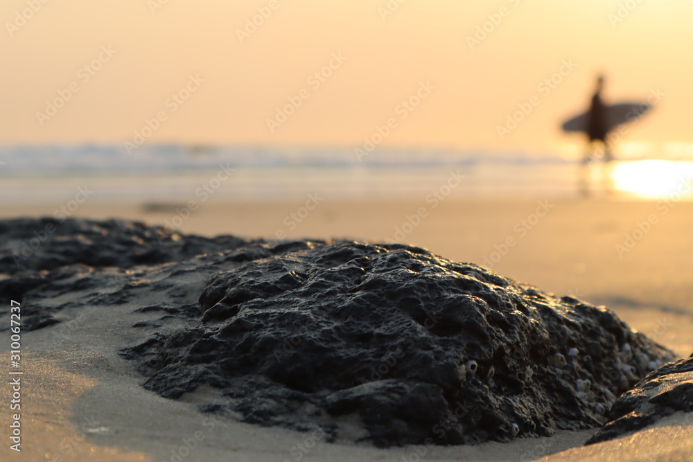 日出，冲浪者剪影背景，岩石和沙子前景