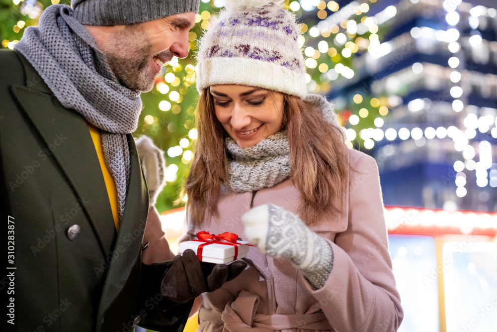 The couple give Christmas gifts against the background of outdoor decorations during an evening walk