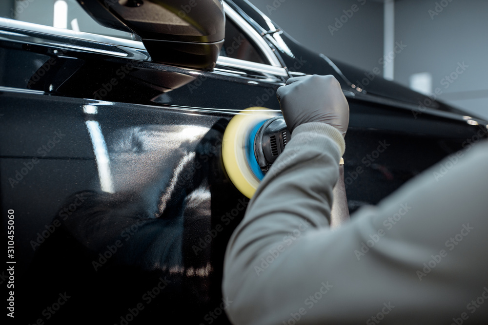 Car service worker polishing vehicle body with special wax from scratches, close-up. Professional ca
