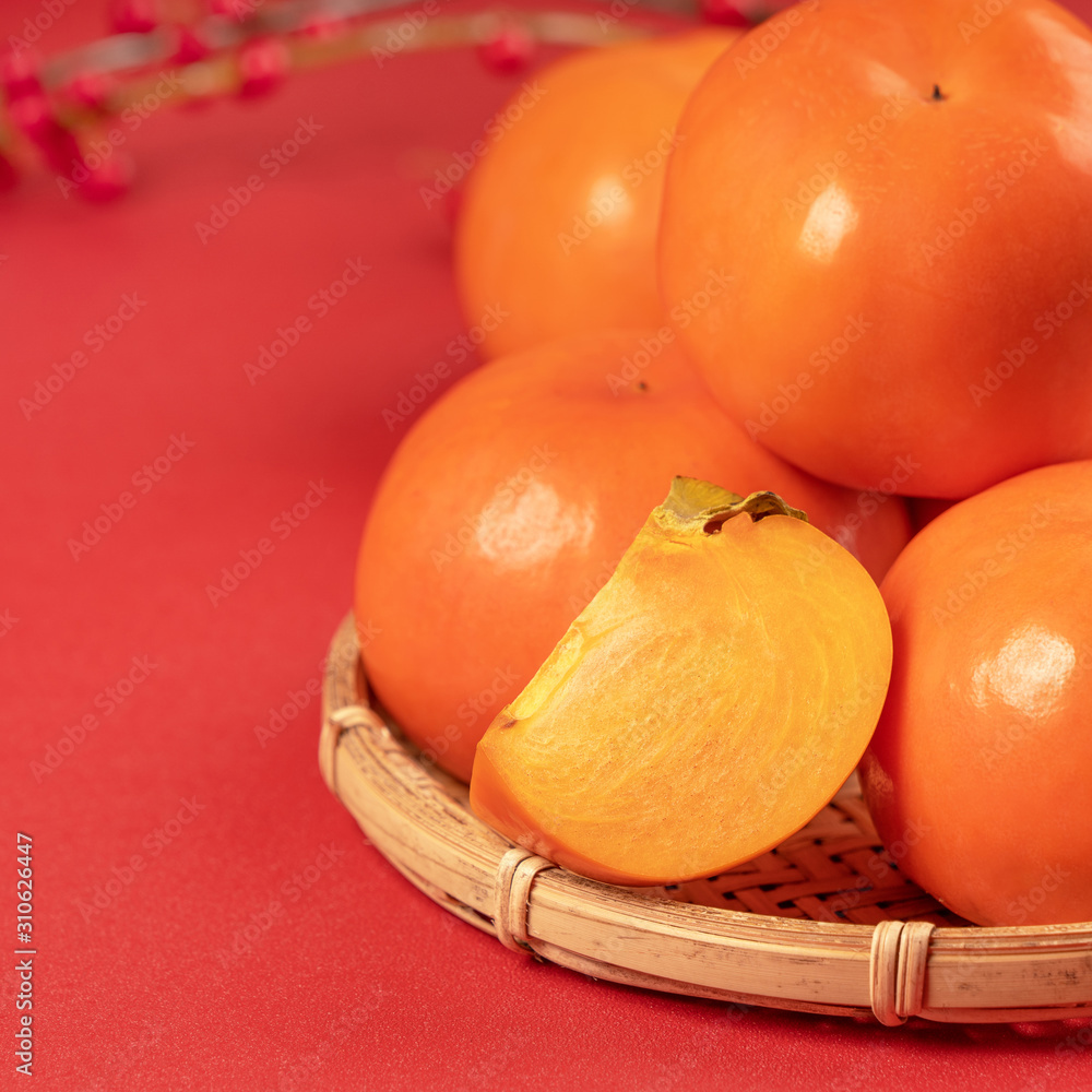 新鲜漂亮的甜柿子切片，红色桌子背景和竹筛分离，中国