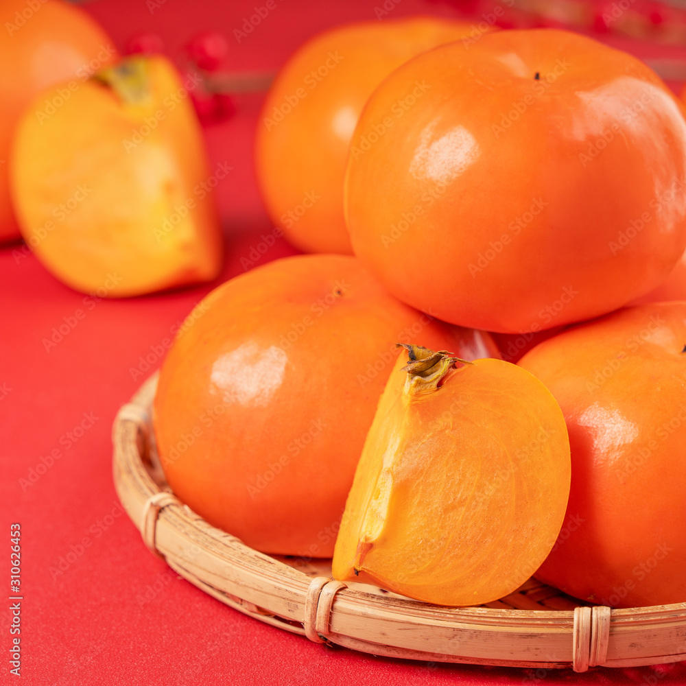 新鲜漂亮的甜柿子切片，红色桌子背景和竹筛分离，中国