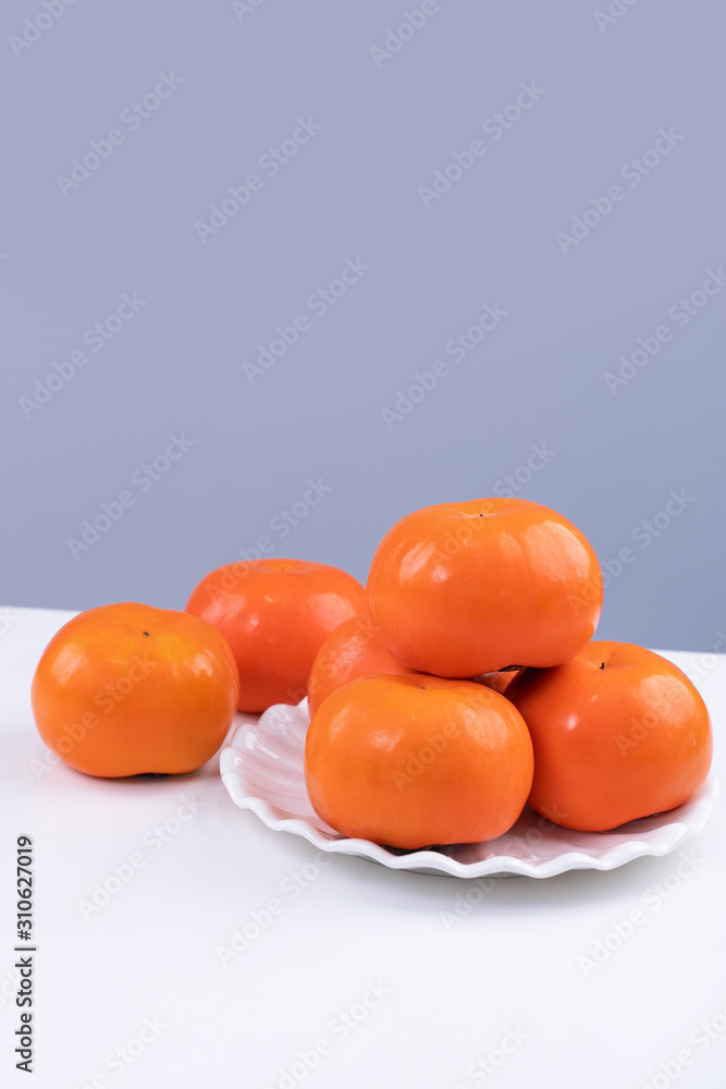 新鲜漂亮的甜柿子切片，被隔离在白色厨房桌子上，背景为灰蓝色