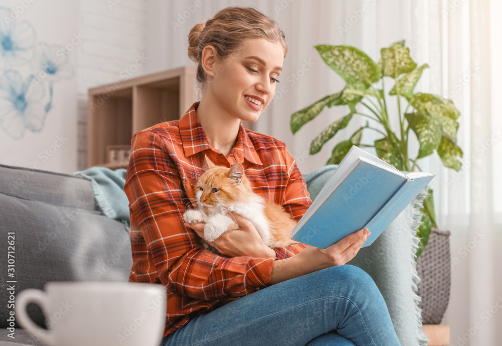 美丽的年轻女人带着可爱的猫在家看书
