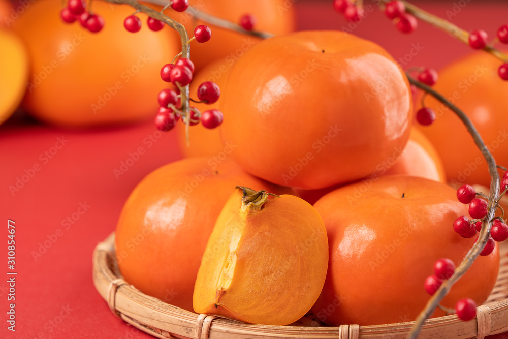 红桌子背景和竹筛上隔离的新鲜漂亮的甜柿子片，中国