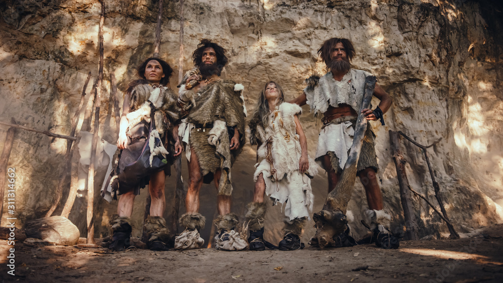 四个猎人聚集的部落，穿着兽皮，拿着石头倾斜的工具，在入口处摆姿势