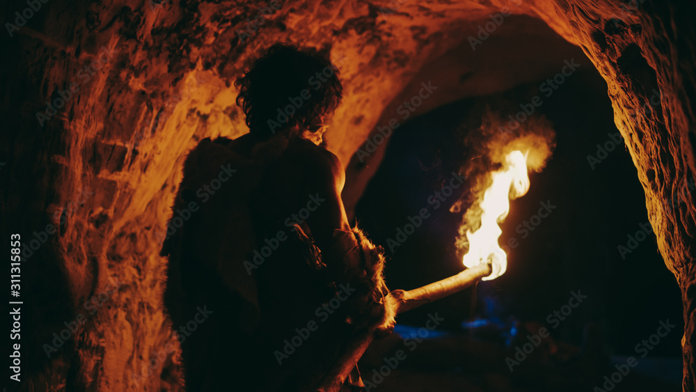 披着兽皮的原始洞穴人夜晚站在洞穴里，手持火把向外张望