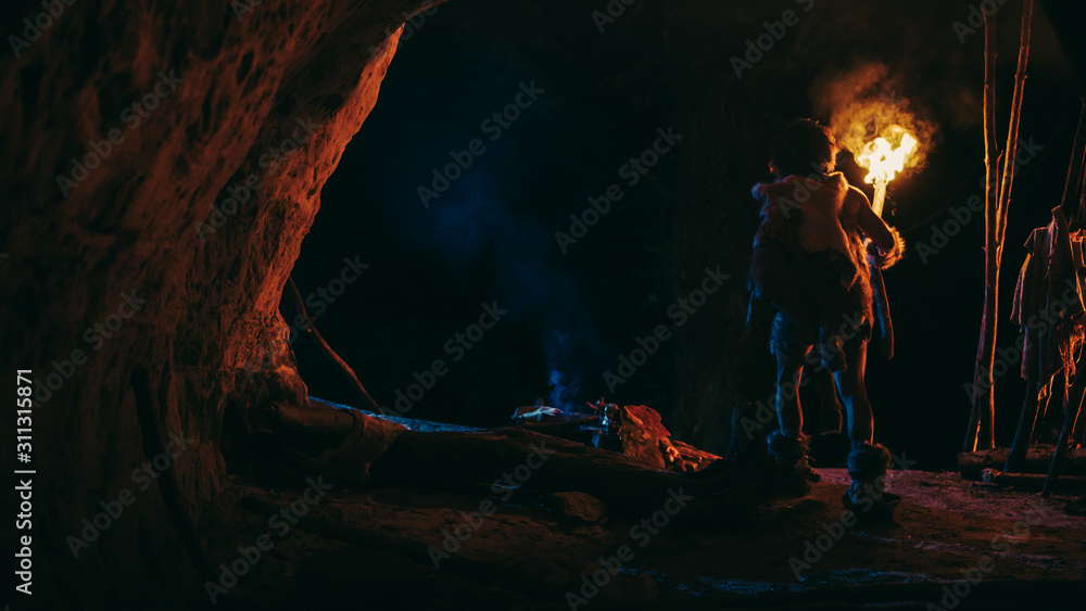 披着动物皮肤的原始洞穴人夜晚站在洞穴中，手持火炬向外张望