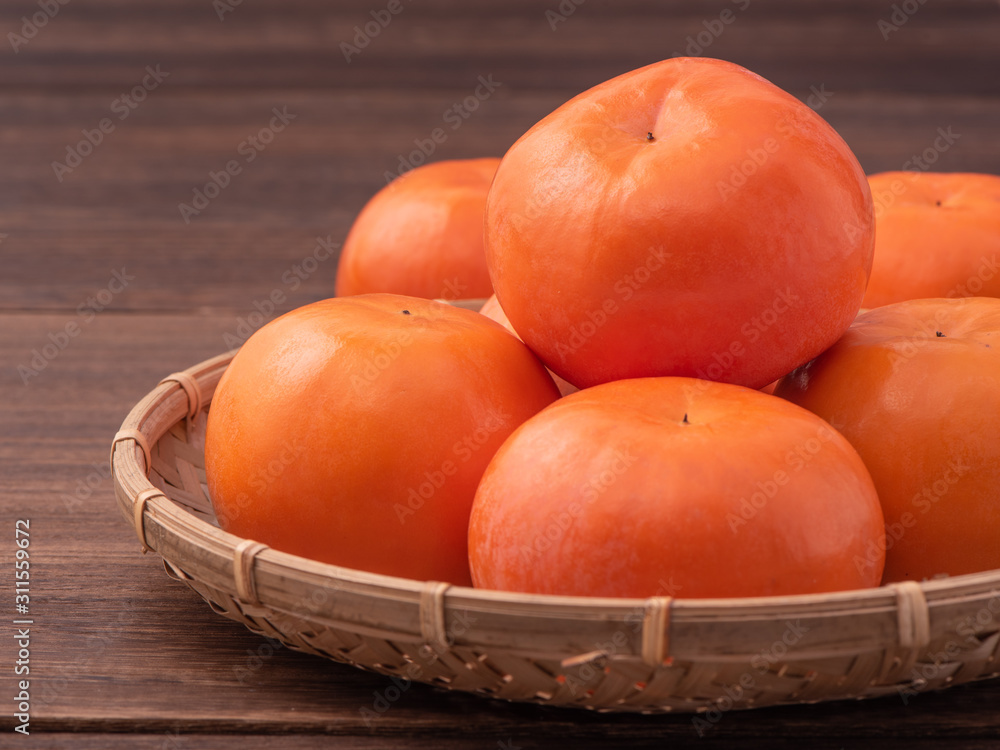 新鲜漂亮的橙色柿子，放在深色木桌上的竹筛上。时令，传统