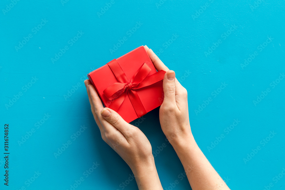 Give a gift on Valentines Day. Women hand hold beautiful red present box on blue background top-dow