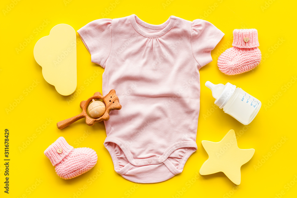 Pink bodysuit for baby girl near childrens things on yellow background top-down