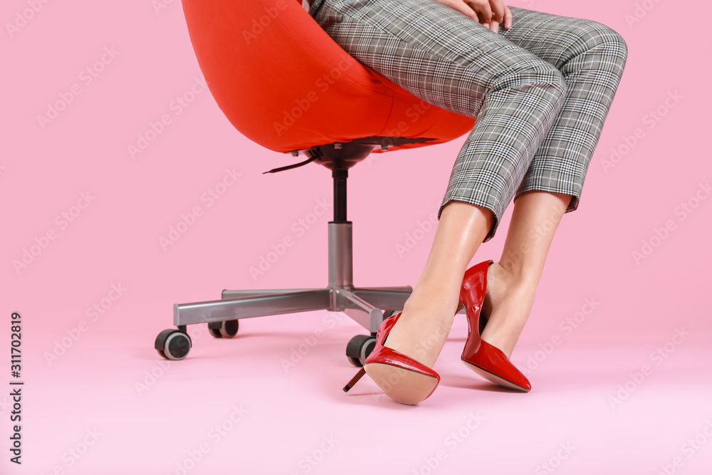 穿着高跟鞋的年轻女子坐在彩色背景下的椅子上