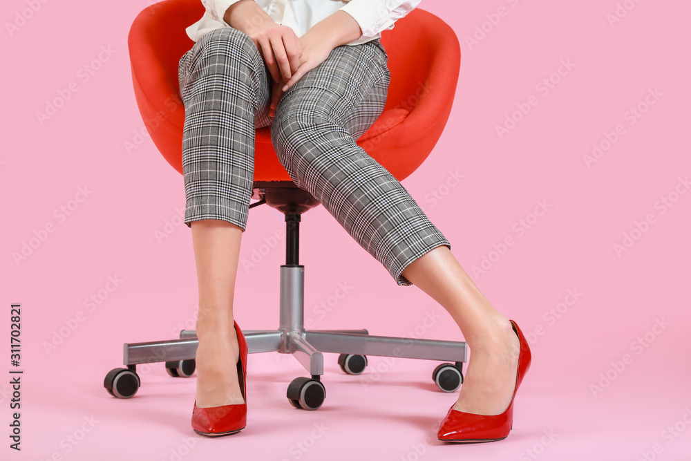 穿着高跟鞋的年轻女子坐在彩色背景下的椅子上