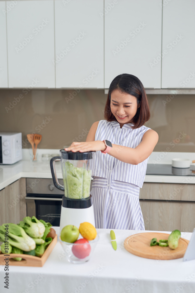亚洲美女在家厨房用果汁机榨汁制作绿色果汁。健康理念