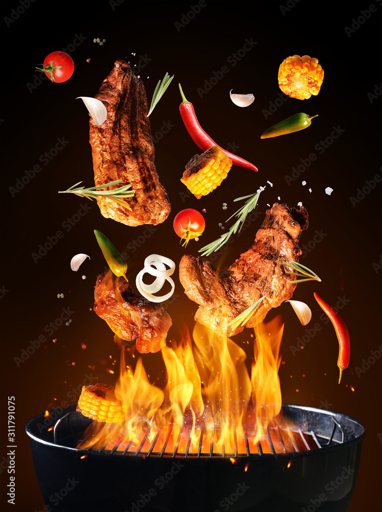 在黑暗背景下，火焰将美味的肉、蔬菜和香料放在烧烤架上