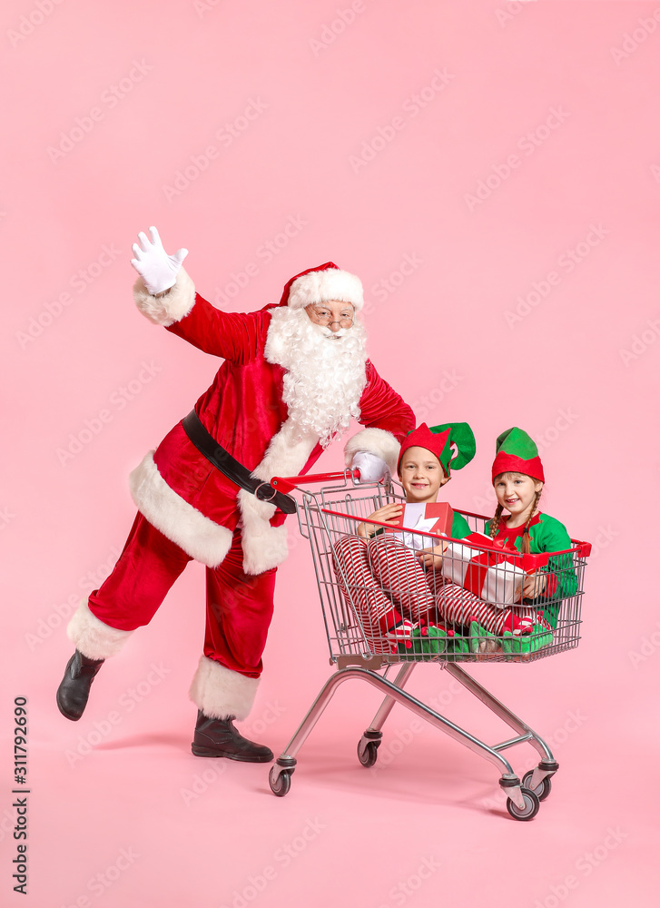 圣诞老人和带着礼物的小精灵坐在彩色背景的购物车里