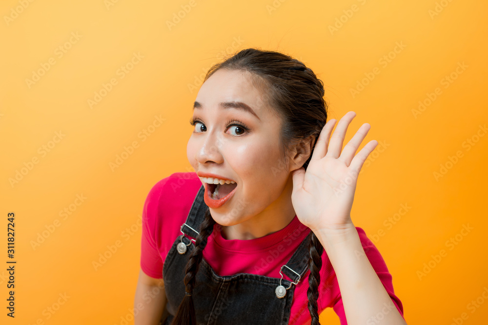 Young teenager Asian girl over isolated yellow background listening gossip by putting hand on the ea