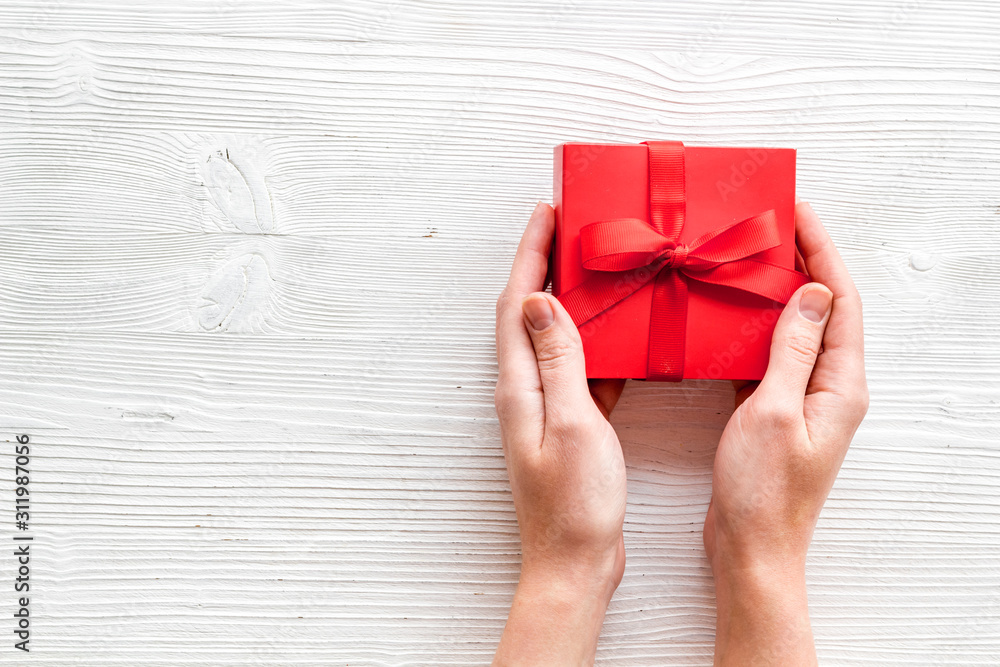 在情人节送一份礼物。女人手拿白色木质背景的漂亮红色礼品盒