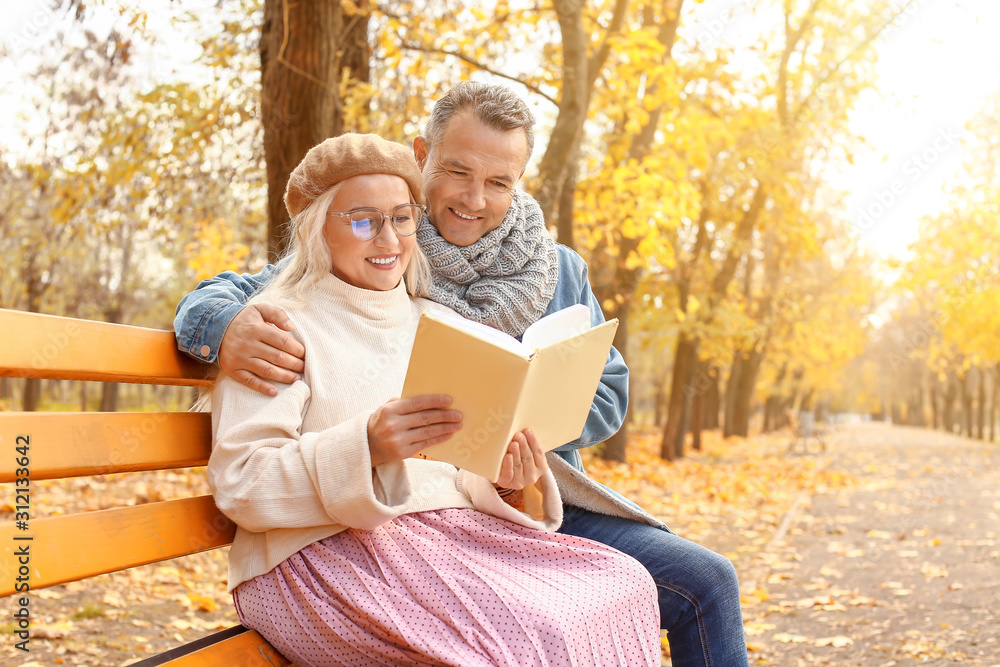 幸福的成熟夫妇坐在秋天公园的长椅上看书