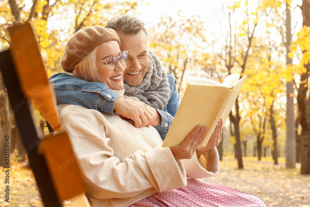 幸福的成熟情侣坐在秋天公园的长椅上看书
