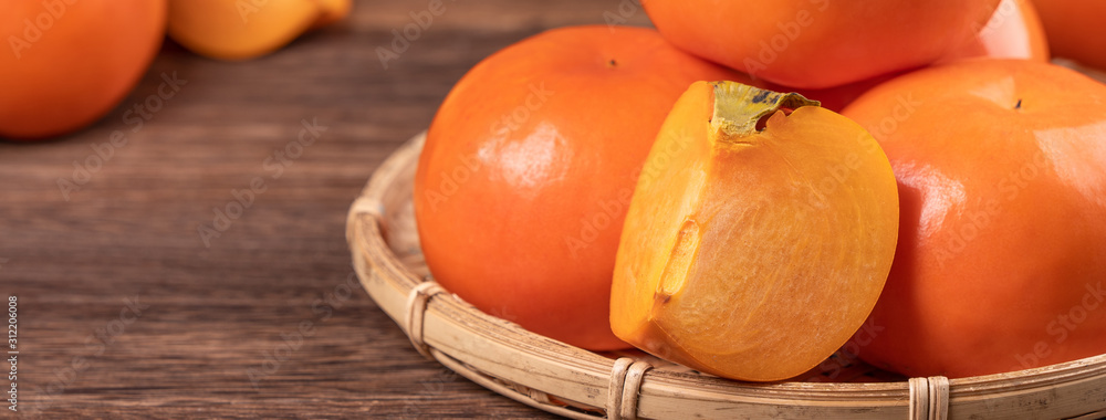 新鲜、美丽的橙色柿子，放在深色木桌上的竹筛上。时令，传统
