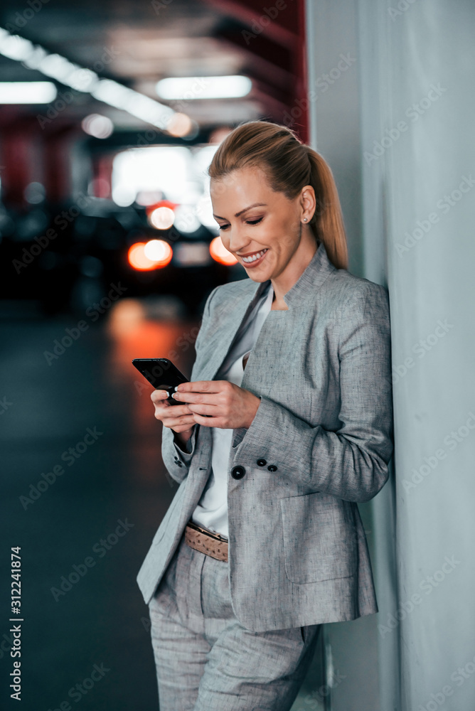 在城市背景下靠在墙上使用智能手机的女商人。