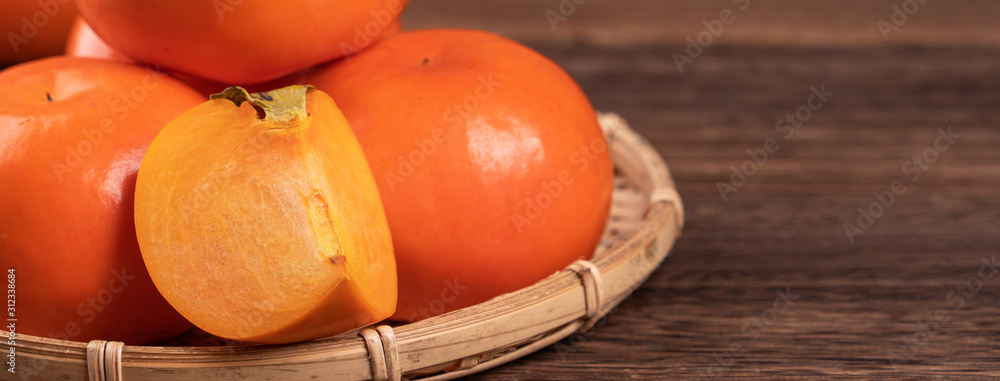 新鲜、美丽的橙色柿子，放在深色木桌上的竹筛上。时令，传统