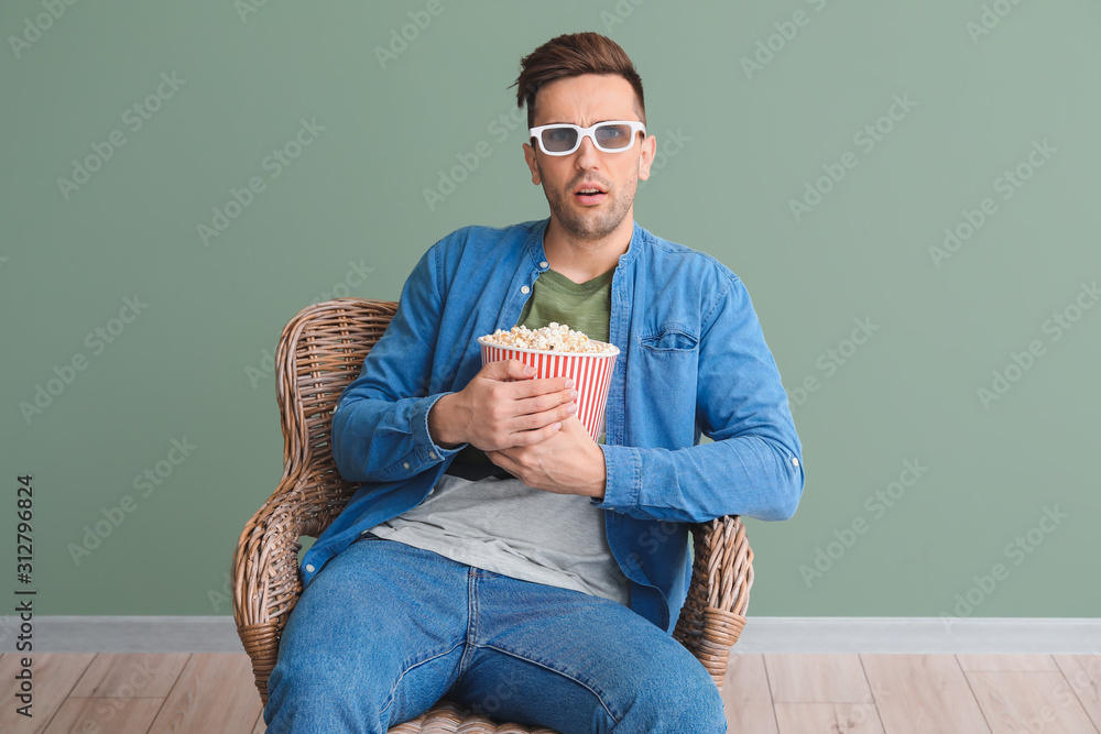 英俊的男人坐在靠近彩色墙的扶手椅上看电影