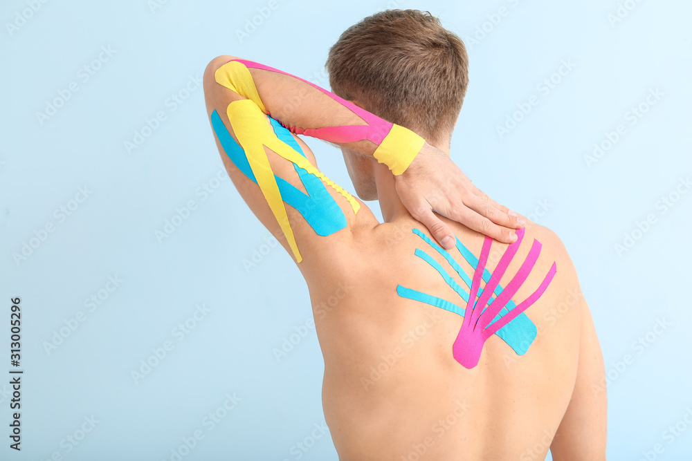 Sporty man with physio tape applied on body against light background