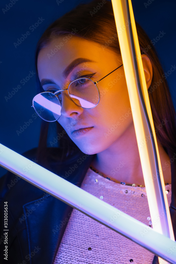 Toned portrait of beautiful woman with neon lamps on dark color background