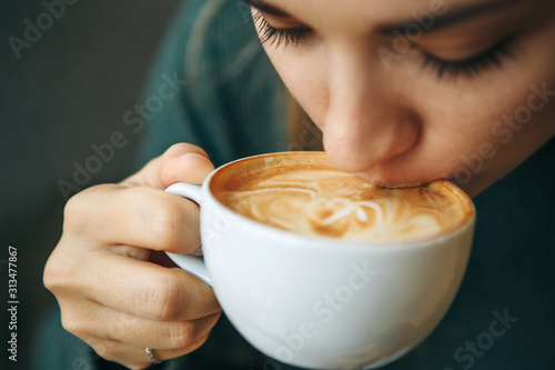 特写女孩正在喝咖啡。她喜欢早上的卡布奇诺或纯白。