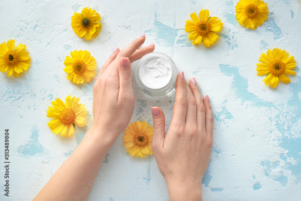 年轻女人的手和一罐彩色背景上有花的奶油