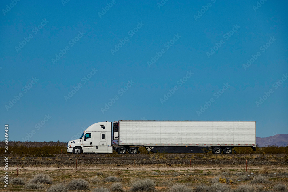CLOSE UP: White semi-trailer truck hauls a container across a desert in the USA.