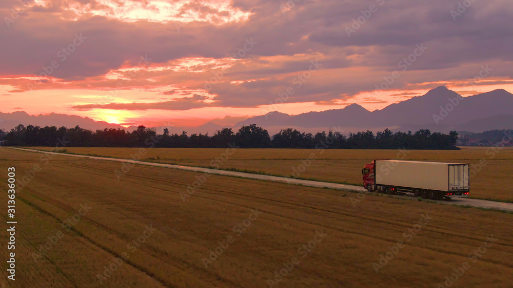 空中飞行：日出时，一辆卡车拖着一个集装箱穿越乡村。