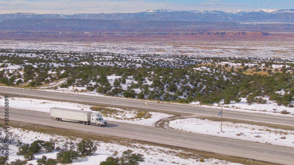 航空：白色卡车沿着风景优美的高速公路运送货物，穿过白雪皑皑的沙漠