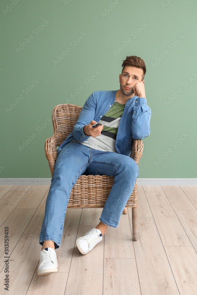 无聊的男人坐在靠近彩色墙的扶手椅上看电视